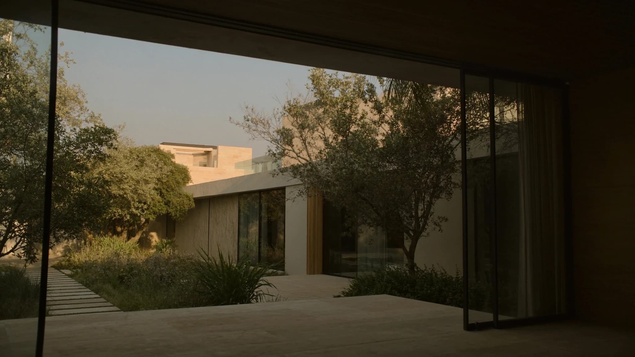 The indoor-outdoor threshold seen from within — sliding glass panels drawn back so stone floor runs uninterrupted into the garden.